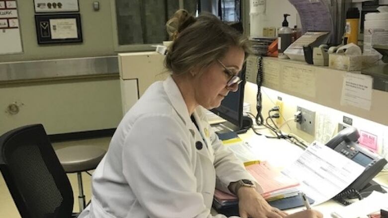 Kirsten Luomala sits at a desk in a medical facility and writes in a patient's file.