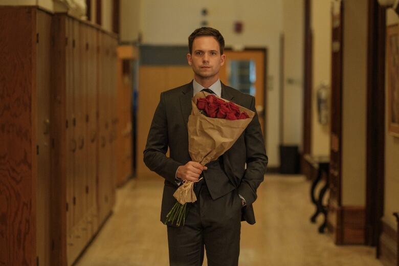 A man in a suit holds a bouquet of roses.