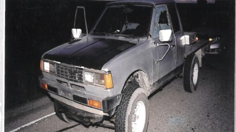 An old truck is pulled over to the side of the road as the sun comes up. The passenger window is rolled down while the driver's window is shattered after it was struck by a bullet.