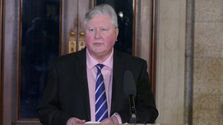 A man with a pink dress shirt stands in front of a microphone.