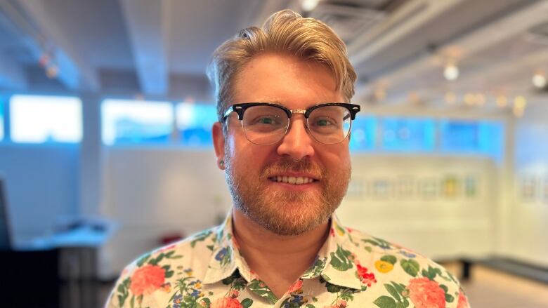 man with glasses in a floral print shirt smiles at the camera