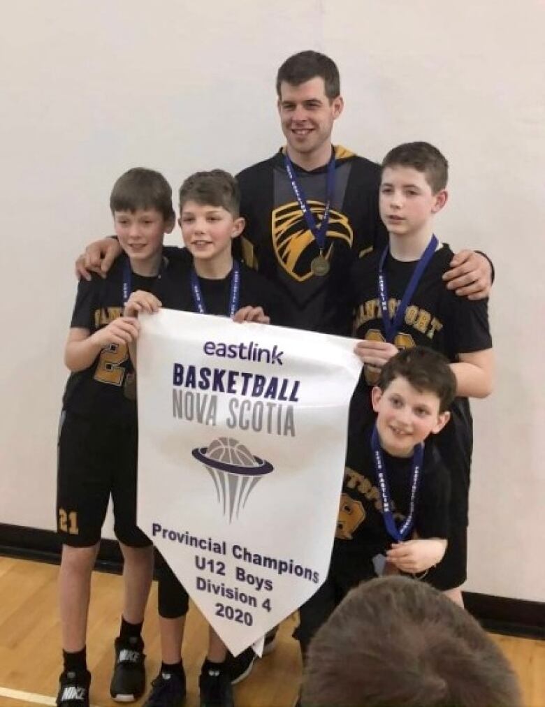 A smiling coach and four youth hold a banner celebrating a basketball championship.