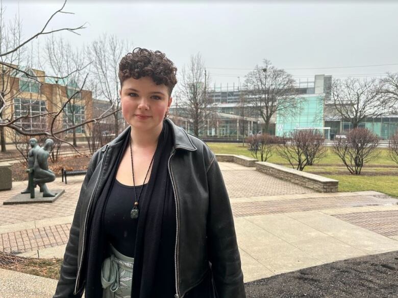 A woman stands in front of trees on a university campus.