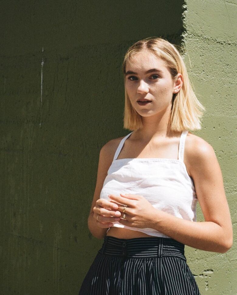 A young woman leans against a wall.