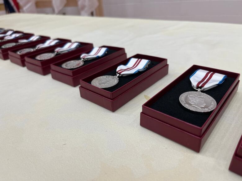 Silver medals hung to ribbons kept in cases are displayed on a table.