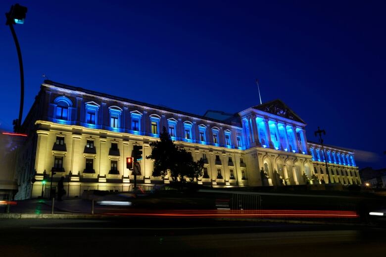 A long, two story building with the top floor lit up blue and the bottom yellow.