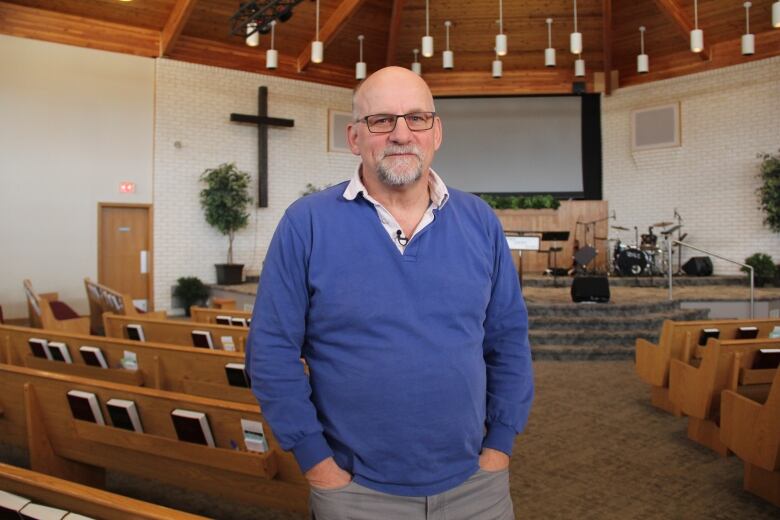 A man in a blue sweater stands in the middle of a church sanctuary to pose for a photo. 