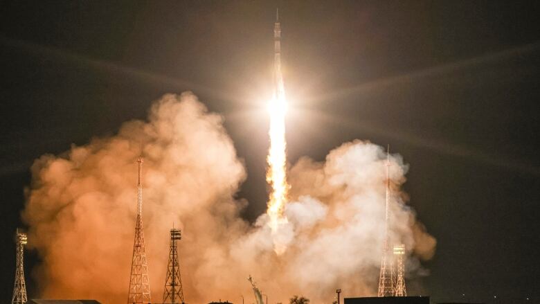 A rocket blasts off at night in a blaze of light and a cloud of smoke