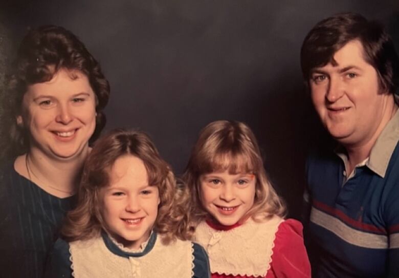 Four people smile  a woman on the left, a man on the right, and two young girls in the centre.