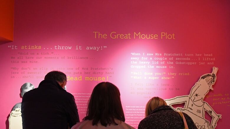 Three adults are shown reading text on a museum wall.