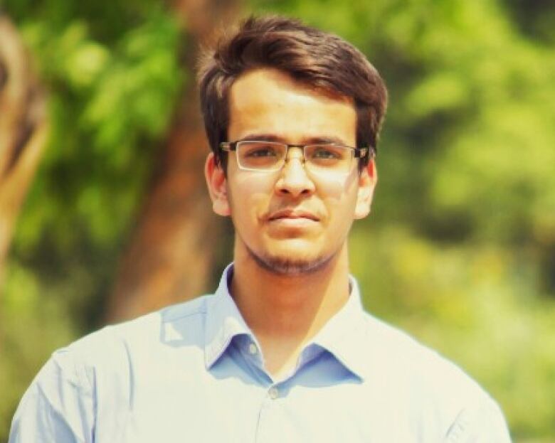 Anklesh Swaroop in little glasses and a suit standing outside on a summer day