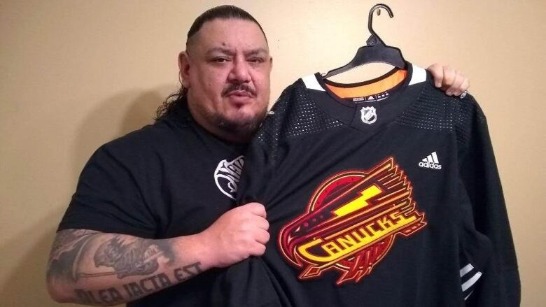 Jay Odjick poses with the Vancouver Canucks warm-up jersey that he designed.