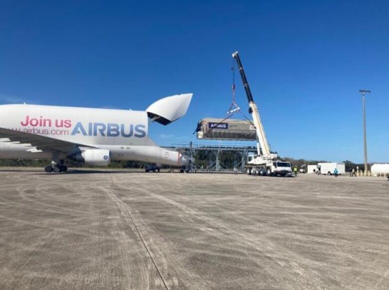 A crane lifts a large piece of equipment into the back of a plane.