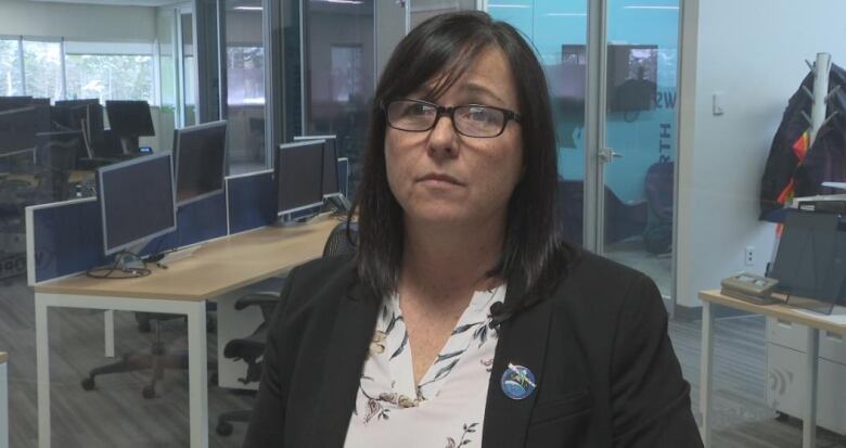 A woman with dark hair and glasses is in front of a table with several dark computer monitors.