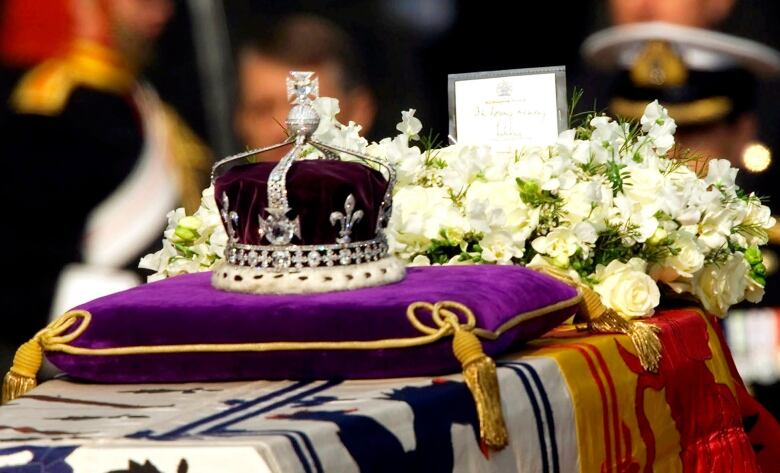 A crown sits on a pillow in front of a bouquet of flowers on top of a coffin.