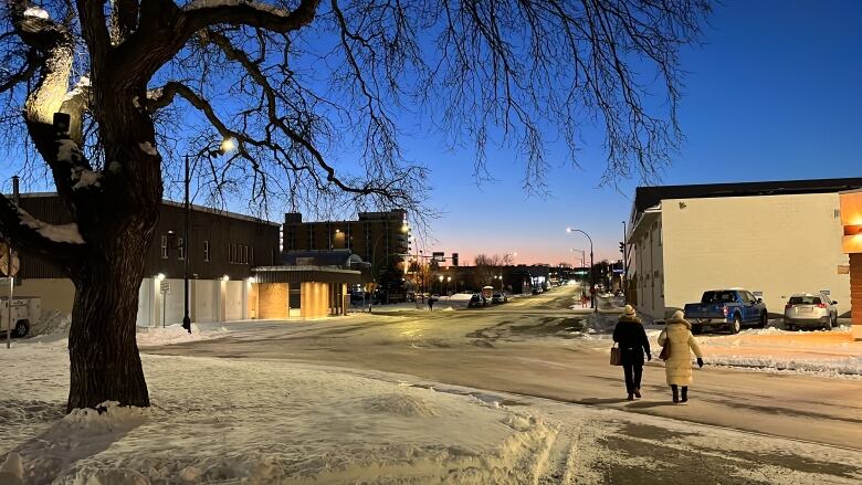 People bundled up in parkas walk across a snow and ice covered road