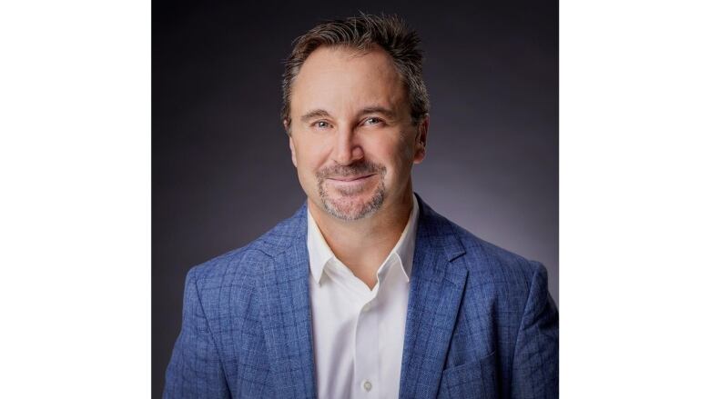 A man with a beard wearing a blue sport jacket and a white dress shirt.