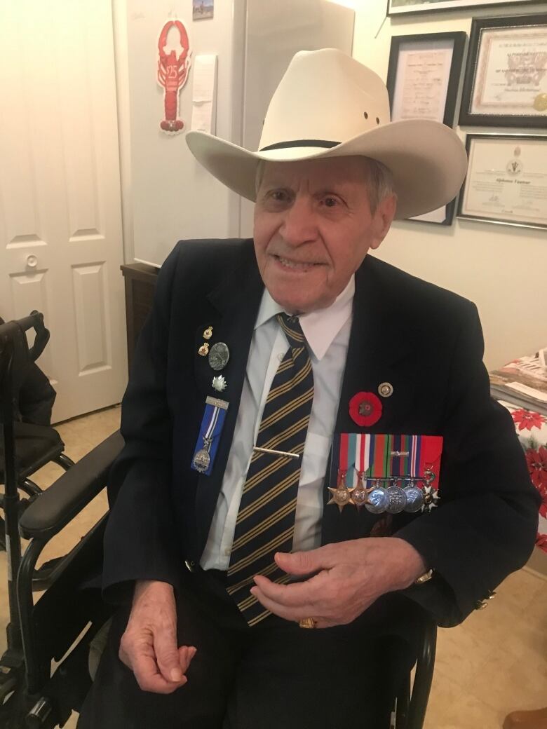 And elderly man wearing a cowboy hat and seated in a wheelchair, with several military medals and a poppy pinned to his jacket. 