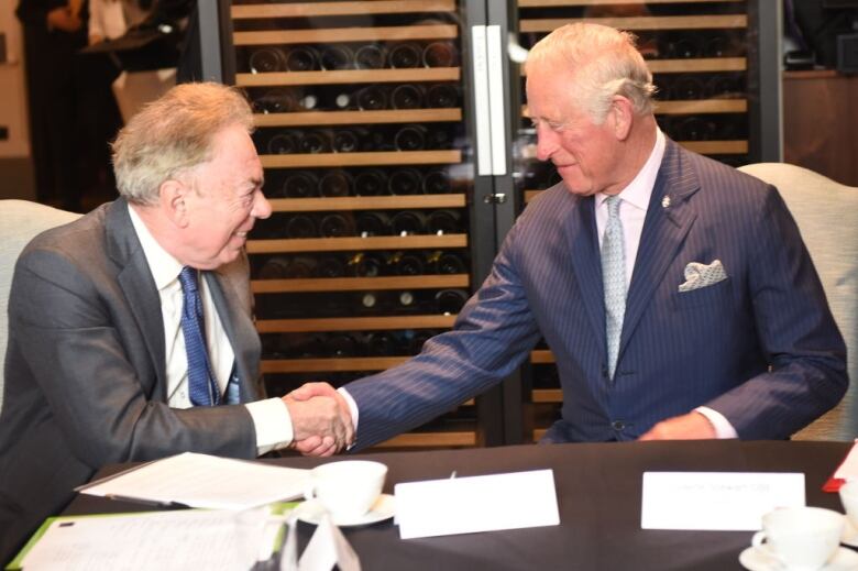 Two people sitting at a table shake hands.