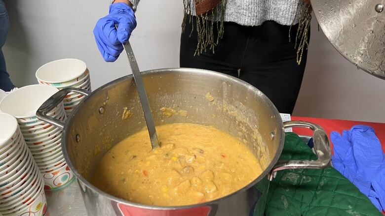 A volunteer stirs a a stainless steel pot full of orange creamy chicken soup