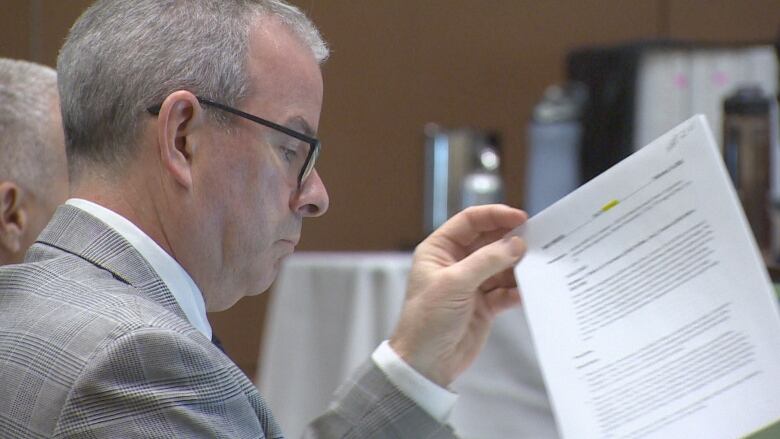 A side profile of a man with black-rimmed glasses flipping through papers