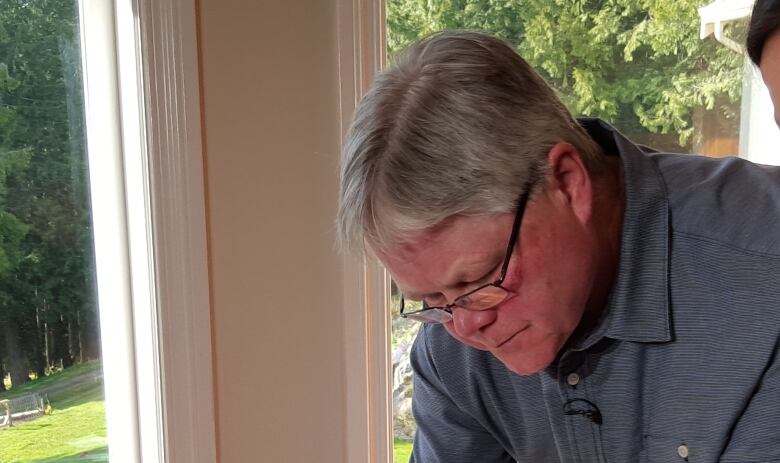 A man with grey hair wearing a blue polo shirt leans over a kitchen table.