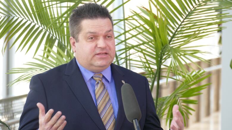 Man stands at podium with arms raised to chest and palms facing up.