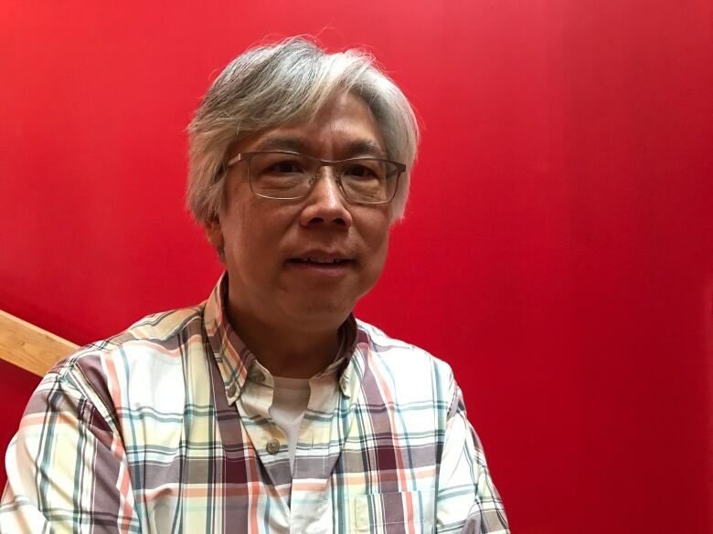 A portrait of a smiling man in glasses in front of a red backdrop.