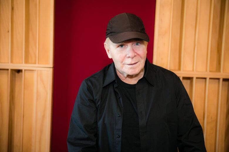 A man dressed in black and wearing a black hat looks at the camera.