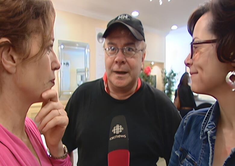 A reporter interviews a man wearing a baseball cap.