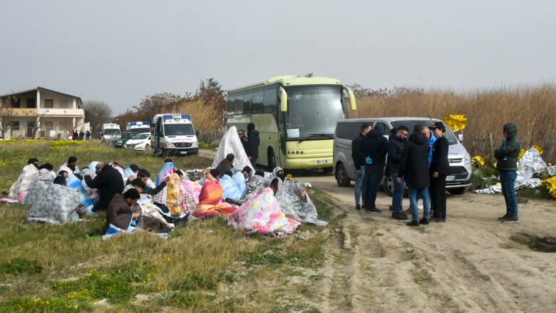 Rescued people sit on the grass, on the left. 