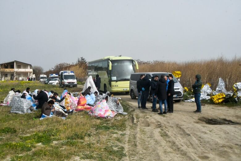 Rescued people sit on the grass, on the left. 