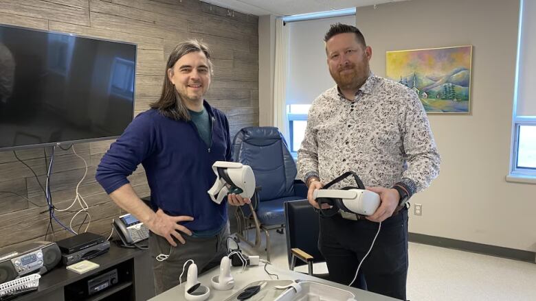 Two men hold white virtual reality headsets.