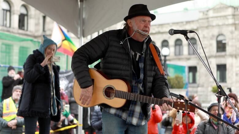 Neil Young is pictured on stage singing and playing guitar. 