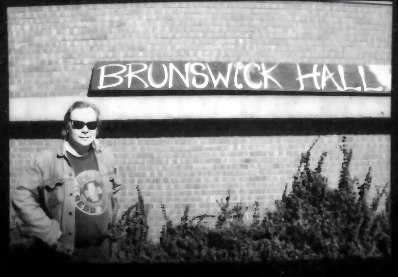 A man wearing sunglasses is shown outside of a brick building with a sign that says, 'Brunswick Hall.'