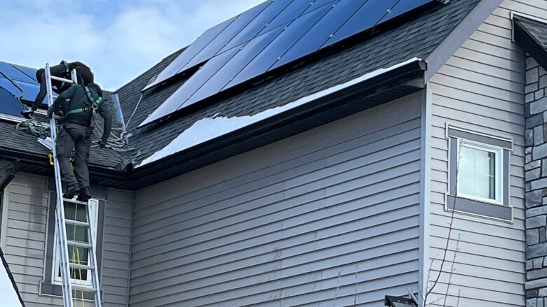 a man on a ladder installs solar panels on a house