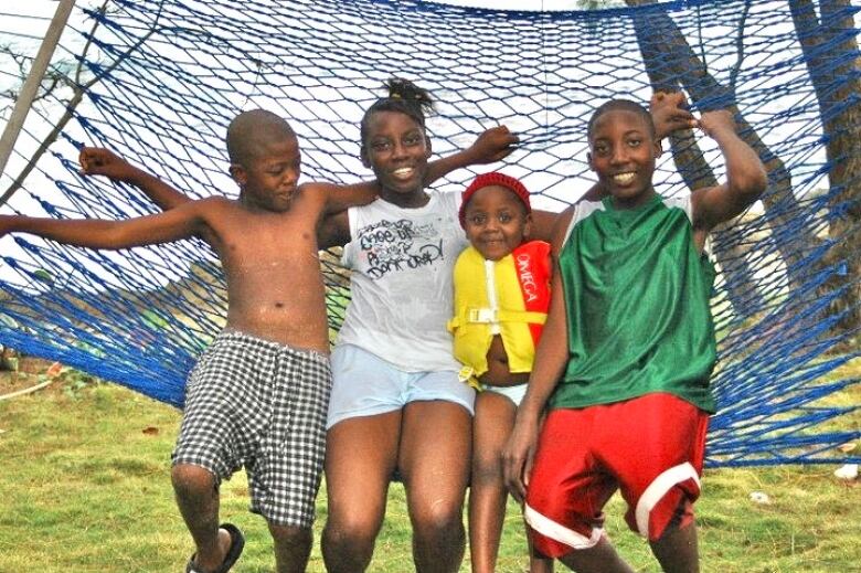 Four children smiling at the camera while swinging on a hammock.