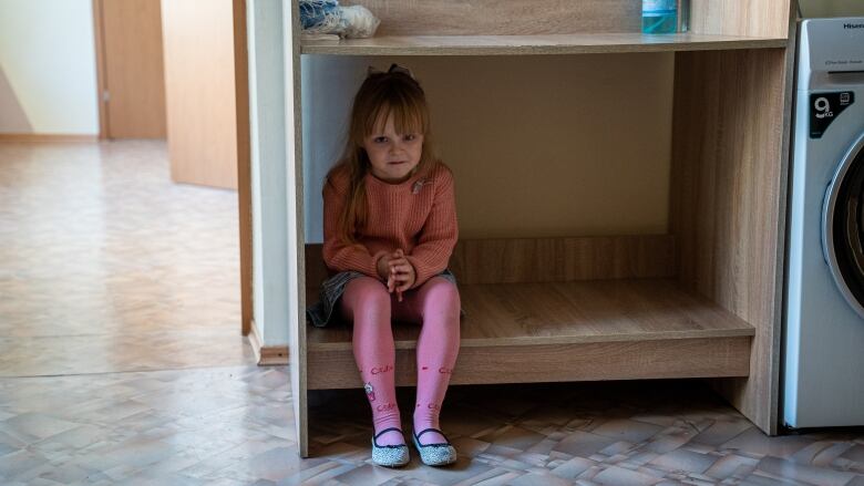 A child sits on a big shelf that is just a few inches off the ground in a laundry room. 