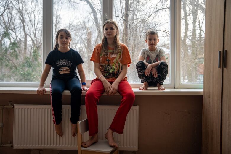 Three kids sit together in front of a window.