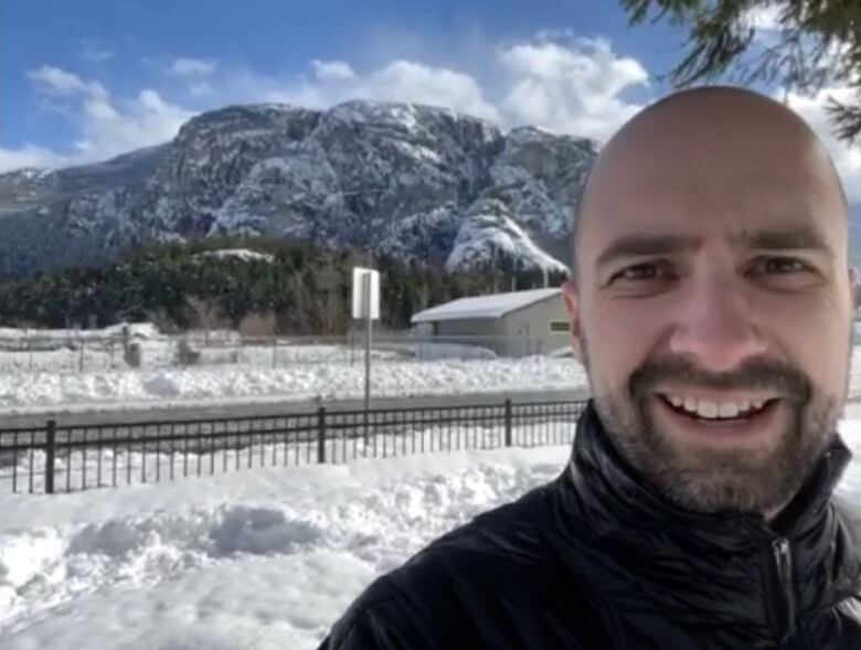 A man is pictured smiling with snow in the background and a snowy mountain. 