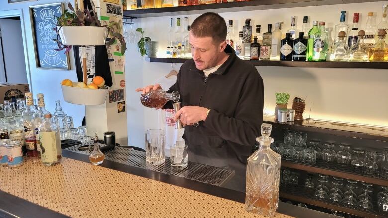 A man is pouring liquid into a shot glass as he mixes a non-alcoholic cocktail behind a bar. 