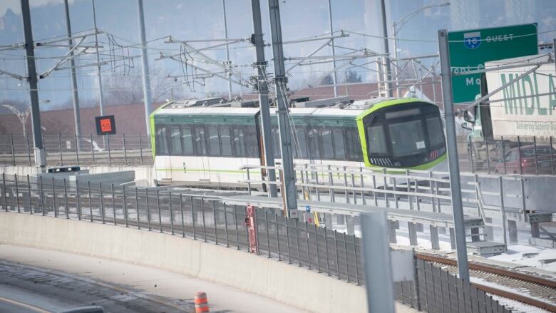 Green and white electric train with two cars on raised tracks