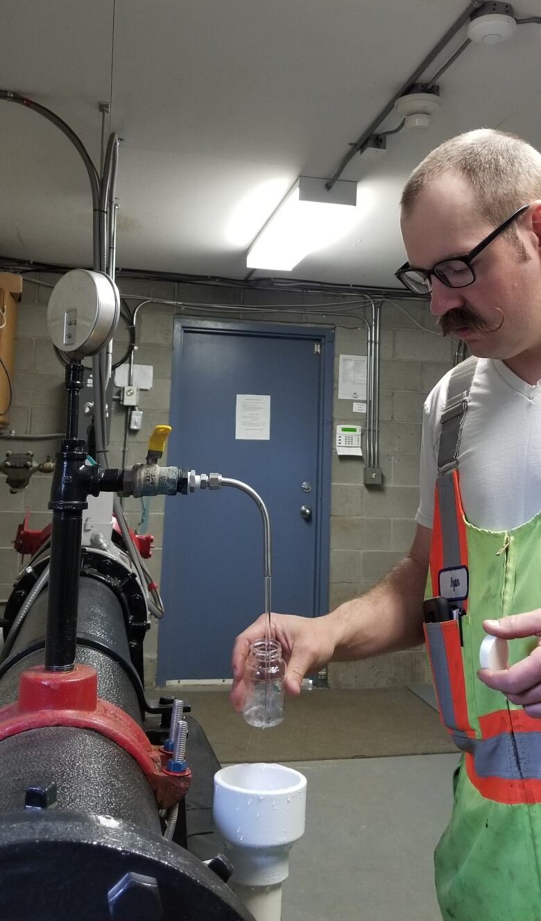 A man fills a small glass jar from a valve on a water pipe.