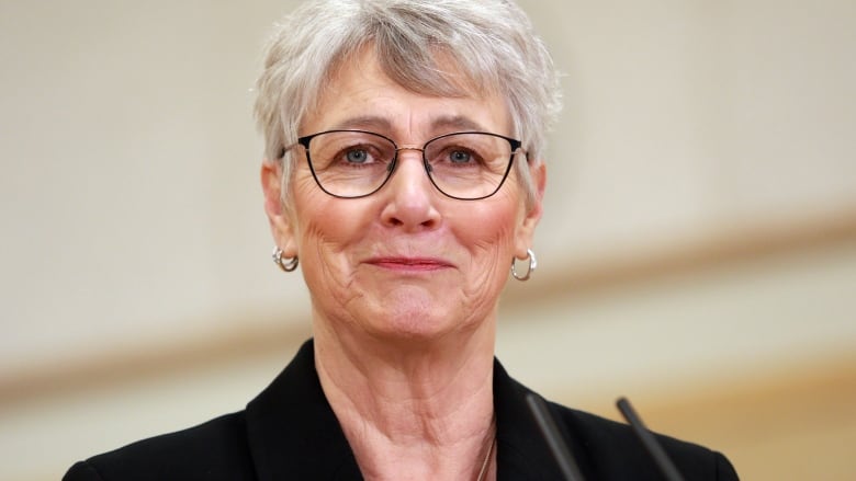 A close-up of a woman with short grey hair and glasses.