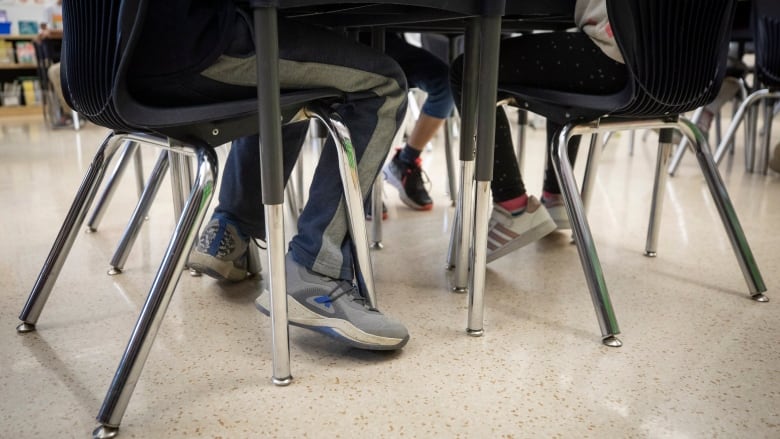 The feet of students under a table in a classroom are shown.