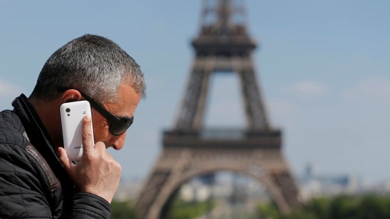 A man talks on a cellphone outdoors, with the Eiffel Tower in the background. 