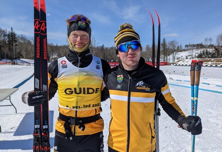 Two men in ski jackets and holding skis smile. 