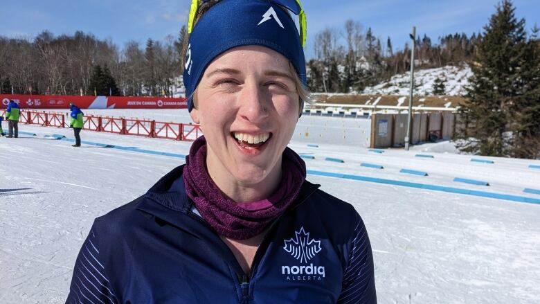 Smiling woman in ski clothes stands on a cross-country ski race route.