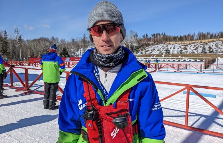 Man in toque, ski wear and goggles stands in front of a cross-country course.