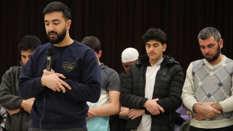 Muslims, lined up in adjacent rows, bow their heads in prayer. 